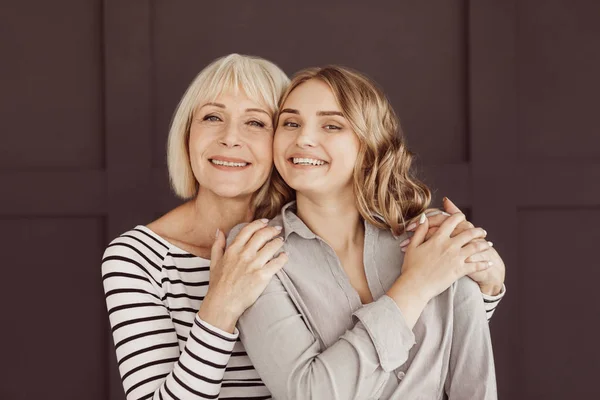 Mujer mayor y joven hija abrazándose contra la pared marrón —  Fotos de Stock