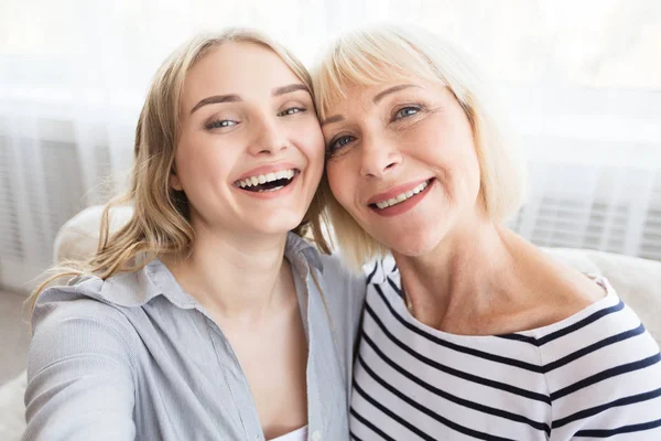 Elderly mother and daughter taking selfie, having fun at home
