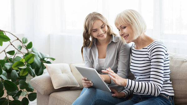 Daughter teaching senior mother to use tablet computer