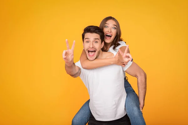 Man giving piggyback ride to woman, showing peace signs — Stok fotoğraf