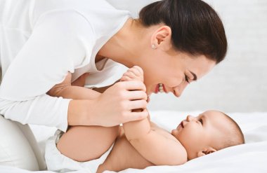 Genç kadın yatakta küçük bebeği ile oynarken
