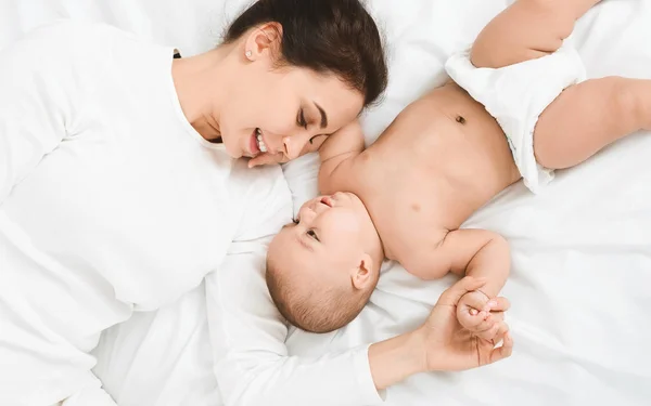 Mutlu anne ve yatakta yatarken şirin küçük yeni doğan bebeği — Stok fotoğraf