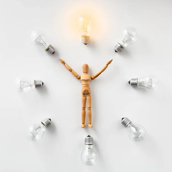 Wooden mannequin carrying glowing light bulb on white — Stock Photo, Image
