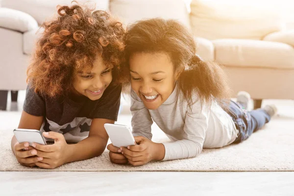 Щасливі маленькі дівчата зі смартфонами лежать на підлозі — стокове фото