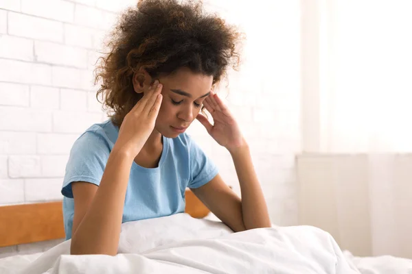 Mujer afroamericana con dolor de cabeza, sentada en la cama —  Fotos de Stock