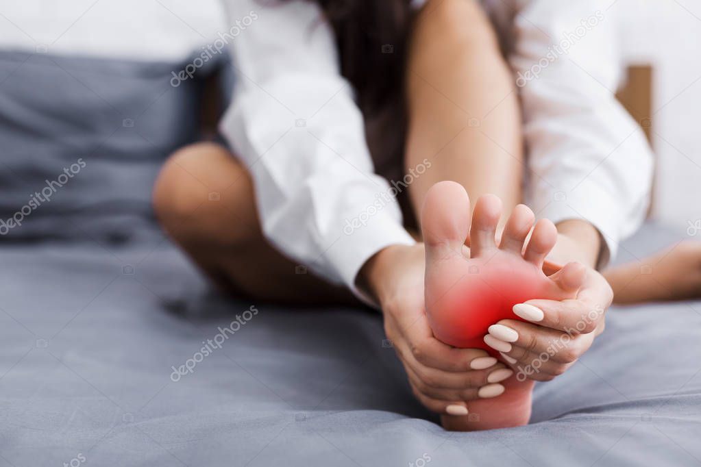 Young woman massaging her foot on bed