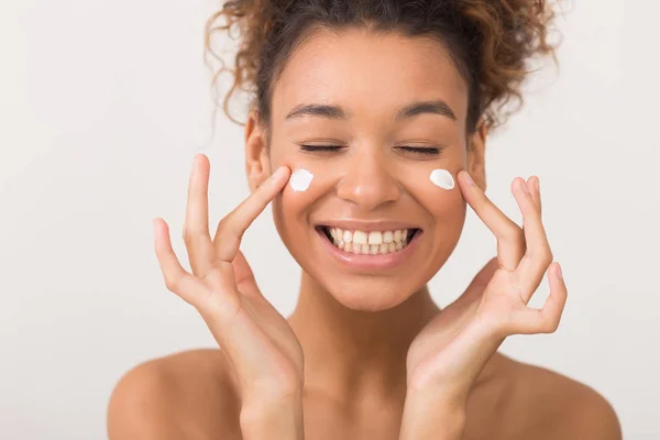 Laughing girl applying moisturizing cream on her face — Stock Photo, Image