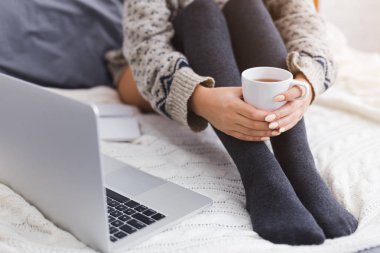 Genç kadının dizüstü bilgisayar ile yatakta çay