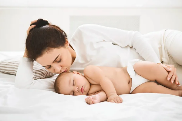 Madre besando a su bebé recién nacido durmiendo en la cama — Foto de Stock