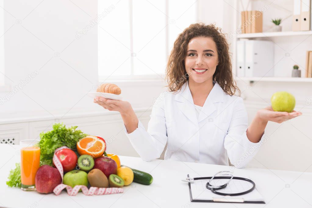 Woman nutritionist holding fruit and croissant in hands