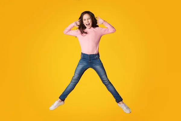 Excited girl jumping and shouting over yellow background — Stock Photo, Image