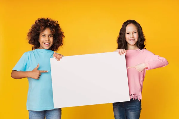 Chicas felices mostrando tablero en blanco y señalándolo — Foto de Stock