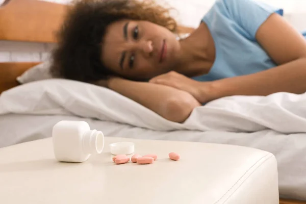 Zieke vrouw kijken pillen, liggend op bed — Stockfoto