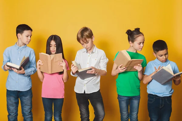 Niños inteligentes leyendo libros cerca de la pared amarilla —  Fotos de Stock