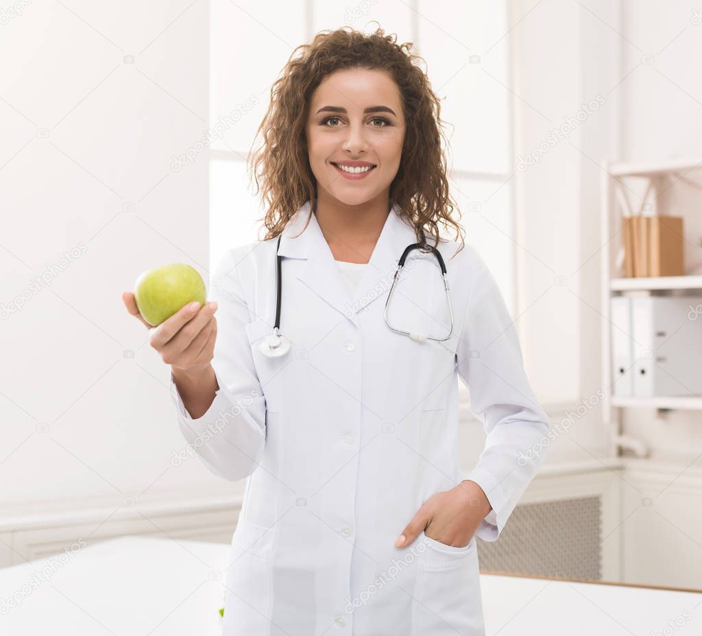 Nutritionist woman offering green apple at camera