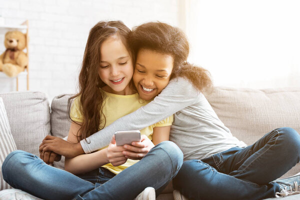 Happy little girls using smartphone and hugging at home