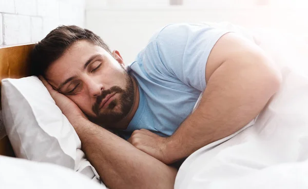 Schöner junger Mann schläft in weißer Bettwäsche — Stockfoto