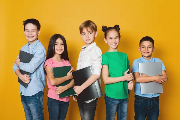 Crianças da escola com cadernos sobre fundo amarelo — Fotografia de Stock