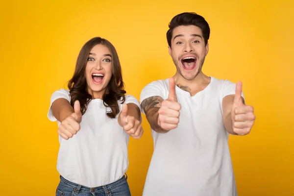 Feliz pareja mostrando pulgares hacia arriba sobre fondo amarillo — Foto de Stock