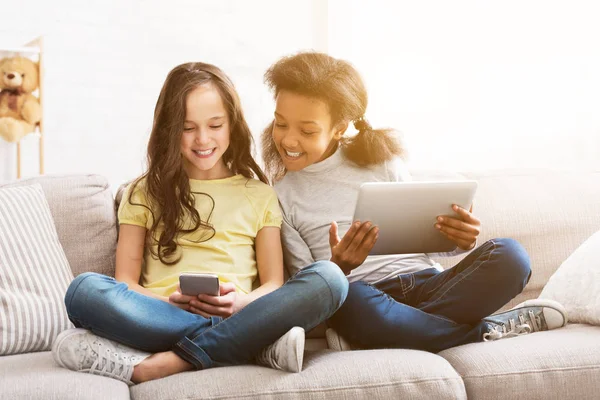 Little friends with gadgets sitting on sofa at home