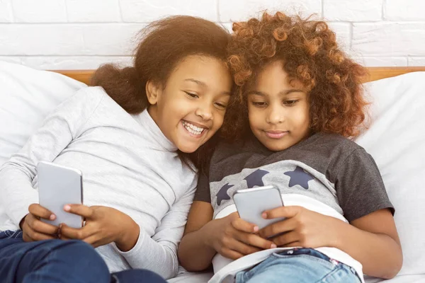 Best friends playing on phones, lying on the bed