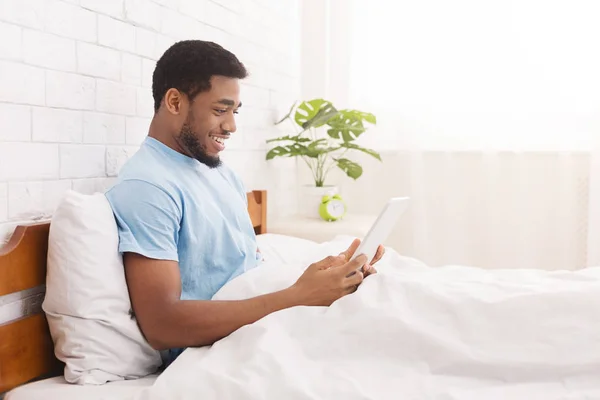 Joven chico millennial utilizando tableta digital en la cama —  Fotos de Stock