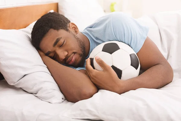 Αφρικανικός-Αμερικανός άνθρωπος στον ύπνο και αγκαλιάζοντας μπάλα ποδοσφαίρου — Φωτογραφία Αρχείου