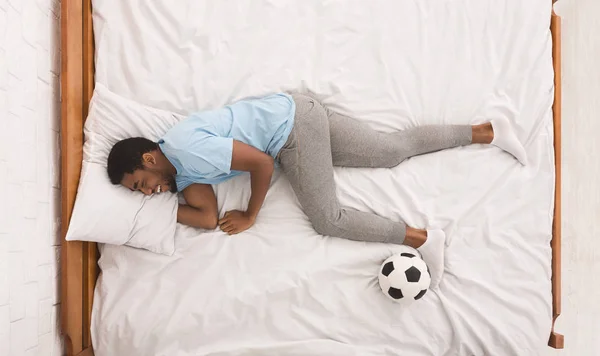 Black sportsman with ball sleeping on bed — Stock Photo, Image