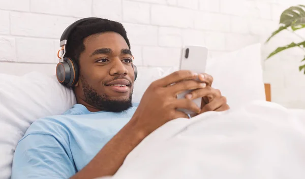 Mann hört Musik mit drahtlosen Kopfhörern im Bett — Stockfoto