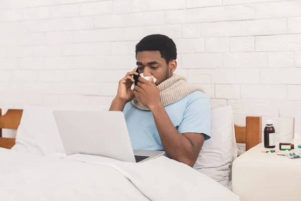 Νεαρός άρρωστος μαύρος άνδρας που εργάζονται για το laptop στο κρεβάτι — Φωτογραφία Αρχείου