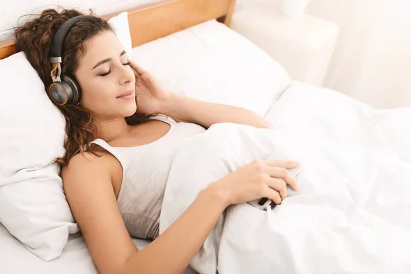 Jeune belle femme se détendre et écouter de la musique au lit — Photo
