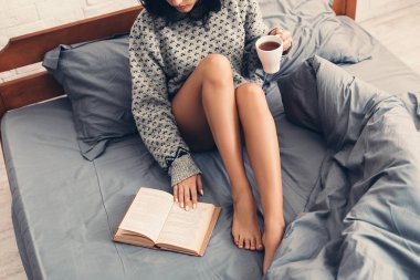 Kadın yatakta kitap ve kahve ile