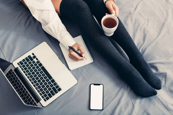 Unrecognizable woman with cup of tea makes notes — Stock Photo, Image