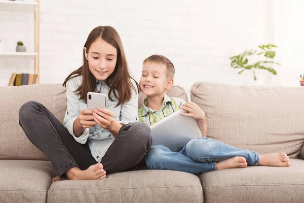 Duas crianças brincando no gadget no sofá em casa — Fotografia de Stock
