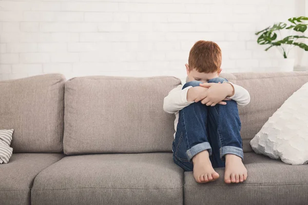 Pojken sitter på soffan och krama hans knä i tår — Stockfoto