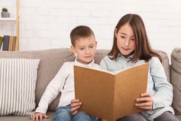 Hermano y hermana leyendo libro en sofá —  Fotos de Stock