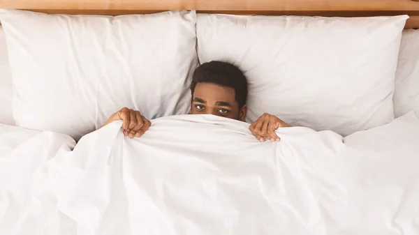 Afrikanisch-amerikanischer Mann versteckt sich im Bett unter Decke — Stockfoto