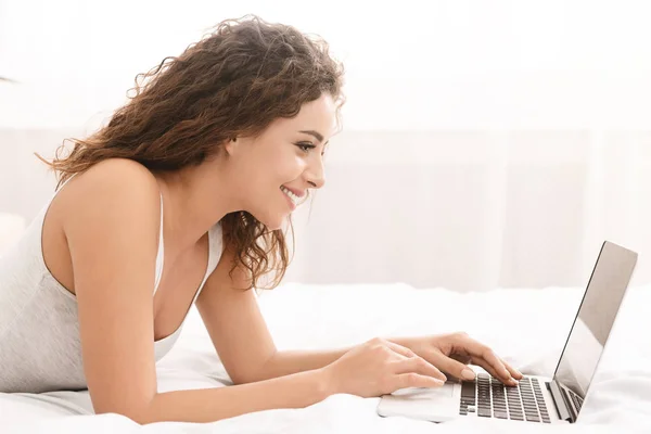 Mujer feliz coqueteando en línea en el ordenador portátil en la cama — Foto de Stock