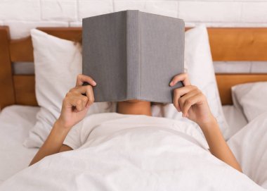 Yatakta yatan kadın kapsayan yüz ve kitap okuma