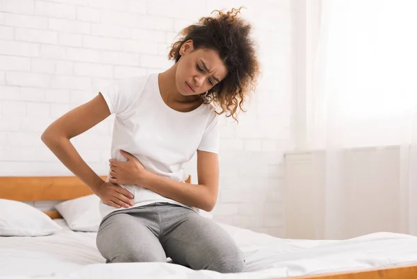 Chica afroamericana que sufre de dolor abdominal en la cama —  Fotos de Stock