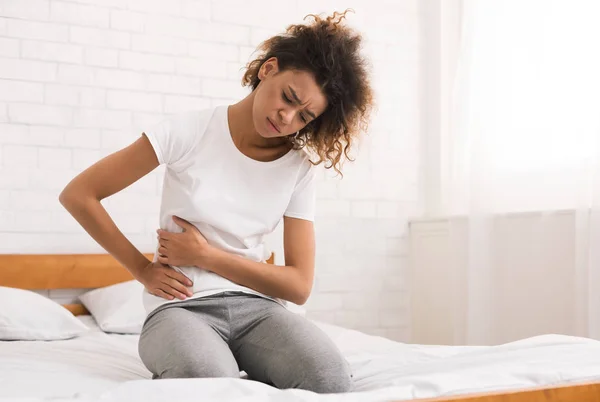 Afro-Amerikaanse meisje die lijden aan pijn in de onderbuik op bed — Stockfoto