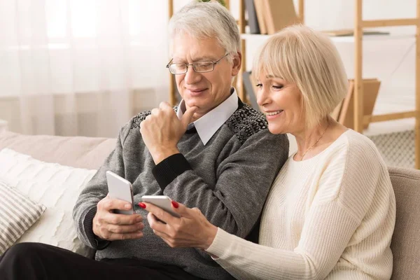 Pareja mayor usando teléfonos inteligentes, viendo fotos en casa — Foto de Stock