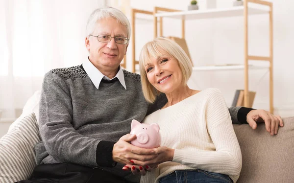 Retirement savings. Senior couple holding piggybank at home — Stock Photo, Image