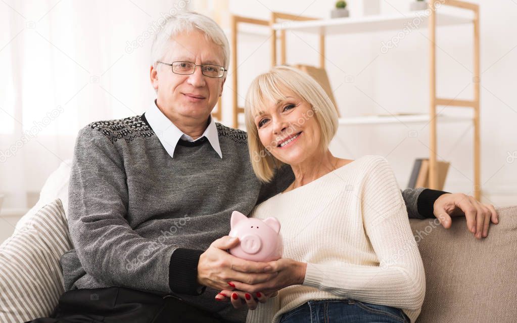 Retirement savings. Senior couple holding piggybank at home