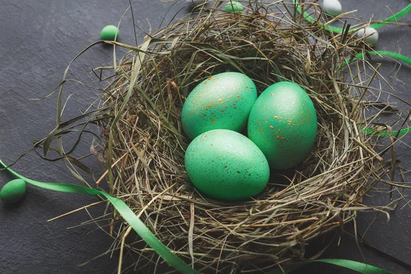 Creative Easter decoration. Green eggs in straw nest, decorated with ribbons, copy space