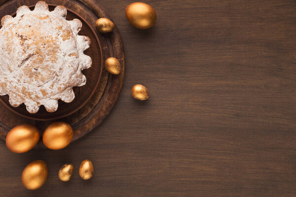 Пасхальный торт и золотые яйца на деревянном столе
