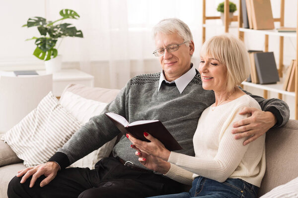 Happy old couple reading book on couch at home