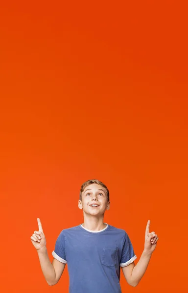 Bonito menino apontando para cima no fundo laranja — Fotografia de Stock