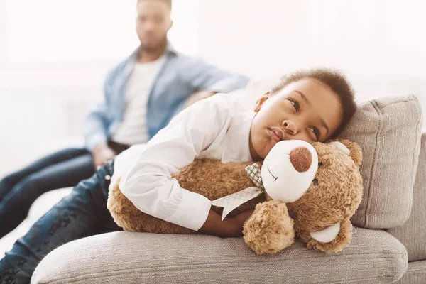 Niña molesta abrazando oso de peluche en el sofá — Foto de Stock