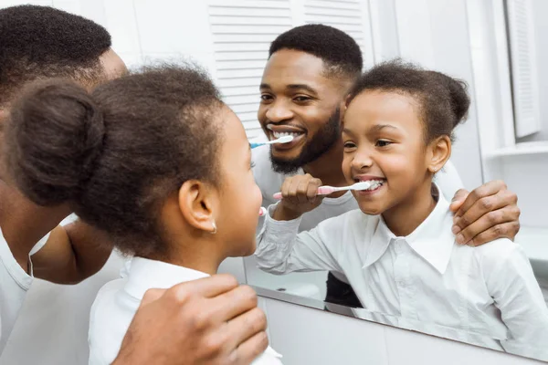 African-american girl brushing teeth together with dad — Stock Photo, Image